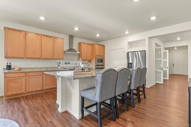 kitchen with recessed lighting, a kitchen breakfast bar, dark wood-type flooring, wall chimney exhaust hood, and appliances with stainless steel finishes