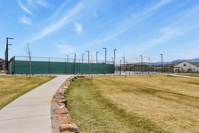 view of property's community with fence, a yard, and a tennis court