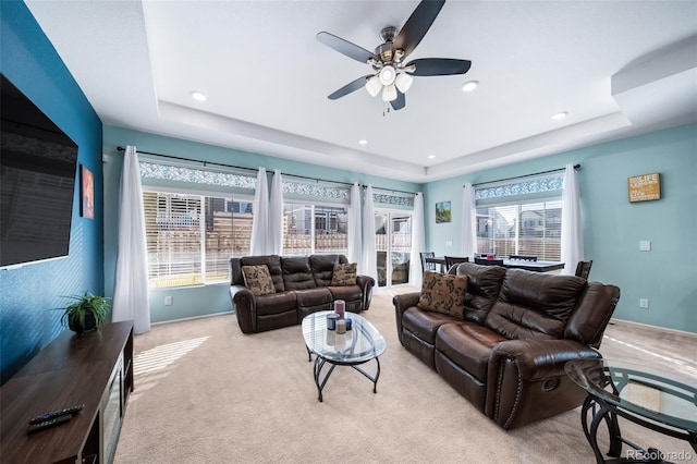 living room featuring a raised ceiling, light colored carpet, and ceiling fan