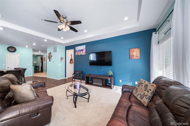 living room with wood-type flooring, ceiling fan, and a tray ceiling