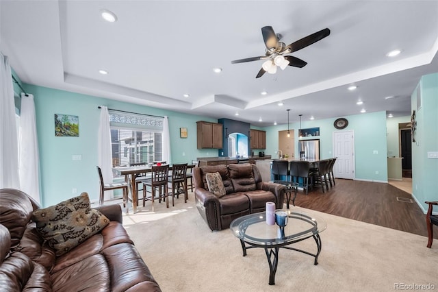 living room with light hardwood / wood-style flooring, a raised ceiling, and ceiling fan