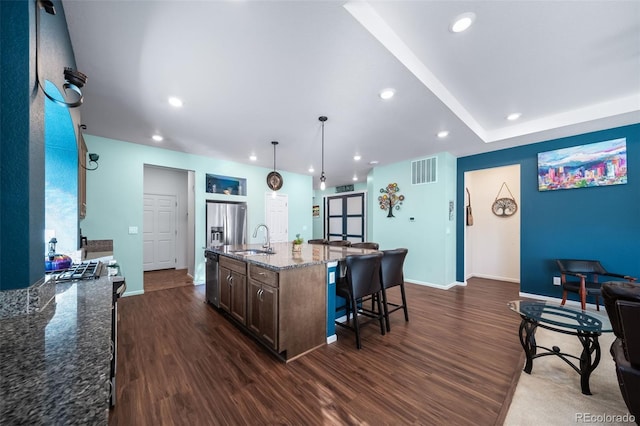 kitchen with stone countertops, pendant lighting, an island with sink, sink, and stainless steel appliances