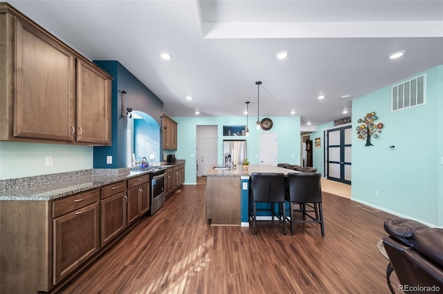 kitchen featuring dark hardwood / wood-style floors, decorative light fixtures, light stone counters, stainless steel appliances, and a center island with sink