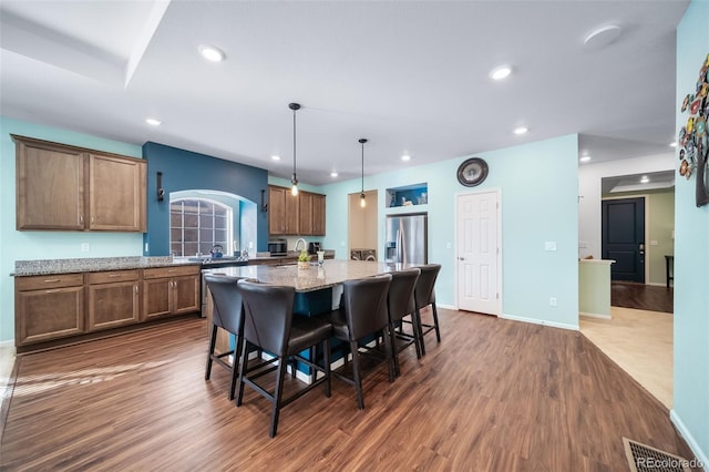 kitchen with pendant lighting, a breakfast bar, light stone countertops, an island with sink, and stainless steel fridge with ice dispenser