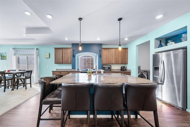 kitchen with hanging light fixtures, stainless steel appliances, sink, and a center island with sink