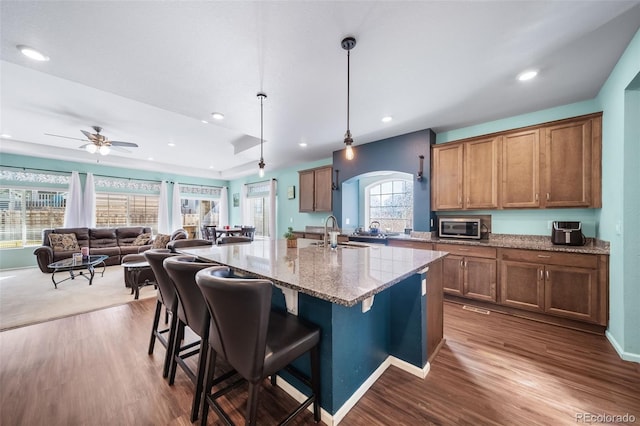 kitchen with pendant lighting, sink, a breakfast bar area, light stone counters, and a center island with sink