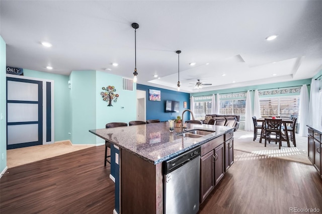 kitchen with dark brown cabinetry, a kitchen bar, stainless steel dishwasher, a raised ceiling, and a kitchen island with sink