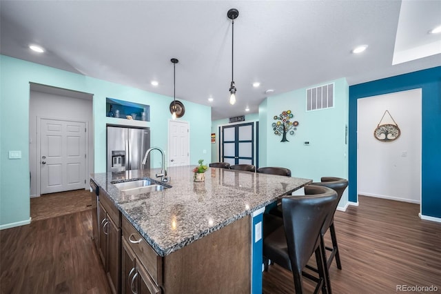 kitchen with sink, stainless steel fridge, a kitchen island with sink, a kitchen breakfast bar, and decorative light fixtures