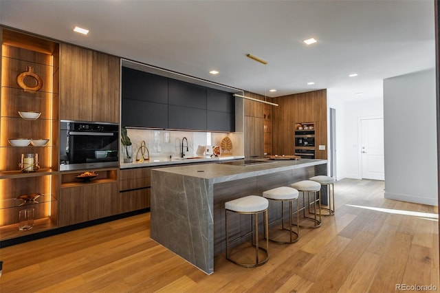 kitchen featuring sink, a kitchen island, black electric stovetop, light hardwood / wood-style floors, and a kitchen bar