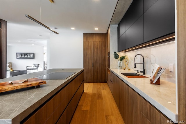 kitchen featuring decorative backsplash, black electric stovetop, sink, and light hardwood / wood-style flooring