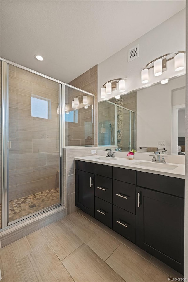 bathroom with double vanity, a sink, visible vents, and a shower stall