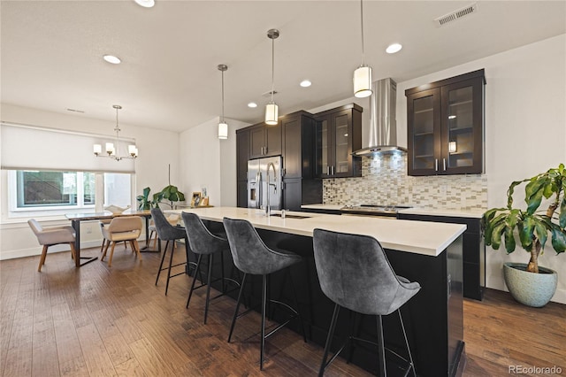 kitchen with a kitchen breakfast bar, backsplash, a center island with sink, visible vents, and wall chimney range hood