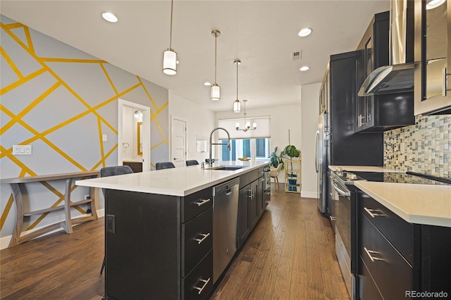 kitchen featuring light countertops, wall chimney exhaust hood, stainless steel appliances, a sink, and dark cabinets