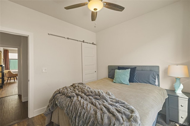 bedroom with baseboards, a barn door, ceiling fan, and wood finished floors
