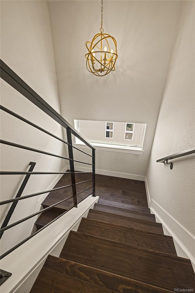 stairs featuring an inviting chandelier, baseboards, and wood-type flooring