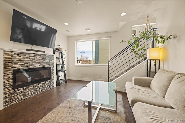 living room featuring stairs, a tiled fireplace, wood finished floors, baseboards, and recessed lighting