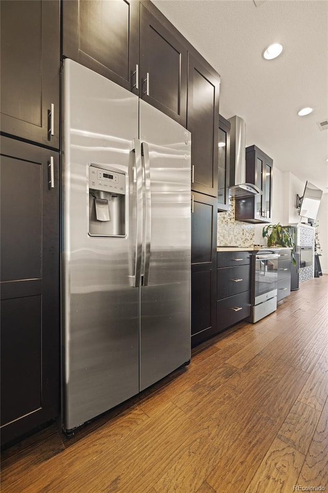kitchen featuring tasteful backsplash, recessed lighting, dark wood finished floors, appliances with stainless steel finishes, and wall chimney exhaust hood