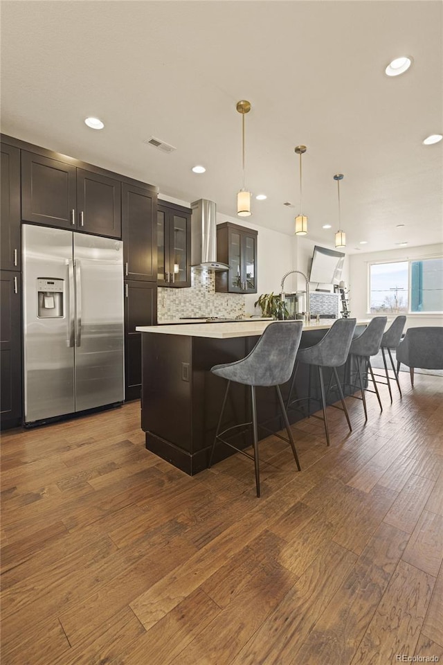 kitchen with light countertops, built in refrigerator, dark wood finished floors, visible vents, and wall chimney range hood