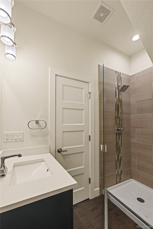bathroom featuring wood finished floors, a sink, a shower stall, and visible vents