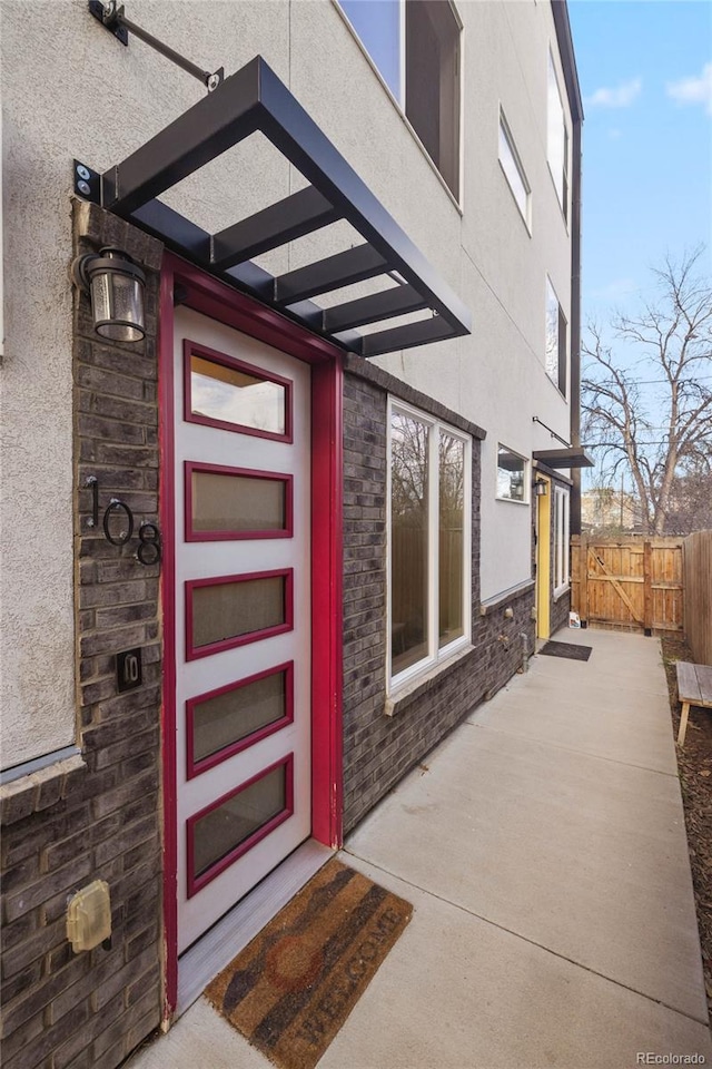 doorway to property featuring stone siding, stucco siding, and fence
