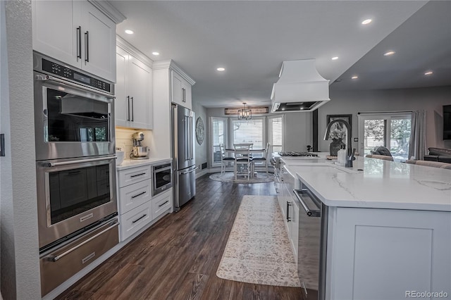 kitchen with appliances with stainless steel finishes, a large island with sink, white cabinets, and light stone countertops