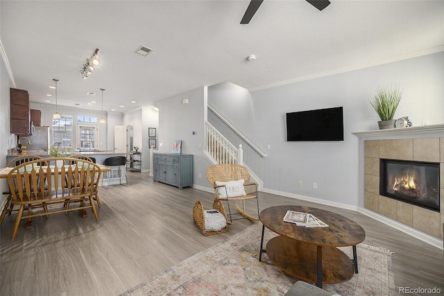 living room featuring ceiling fan, light wood-type flooring, ornamental molding, and a tiled fireplace