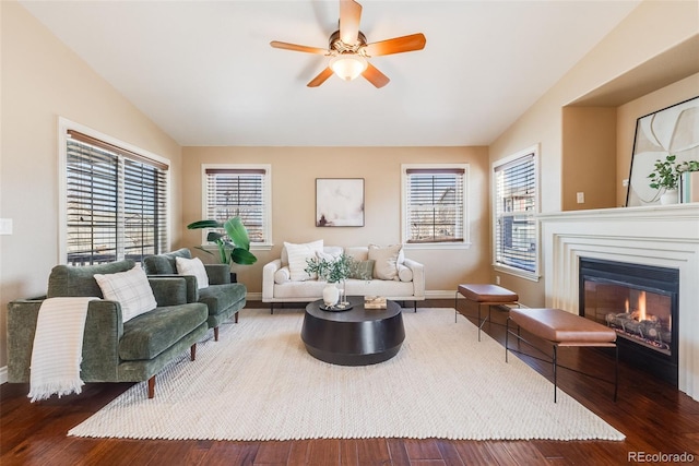 living room with wood finished floors, baseboards, a ceiling fan, vaulted ceiling, and a glass covered fireplace