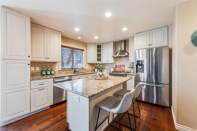 kitchen with a breakfast bar, dark wood finished floors, appliances with stainless steel finishes, wall chimney range hood, and a center island