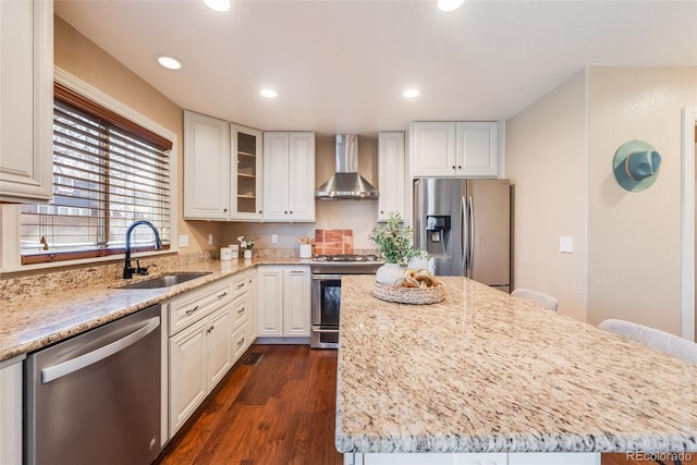 kitchen with a sink, light stone counters, a center island, stainless steel appliances, and wall chimney exhaust hood