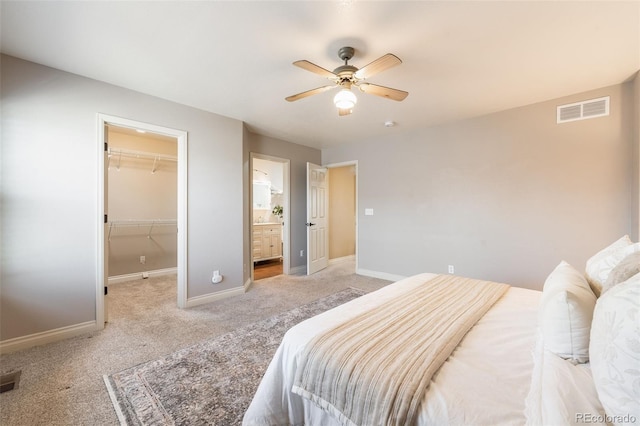 bedroom featuring visible vents, baseboards, light colored carpet, and a walk in closet