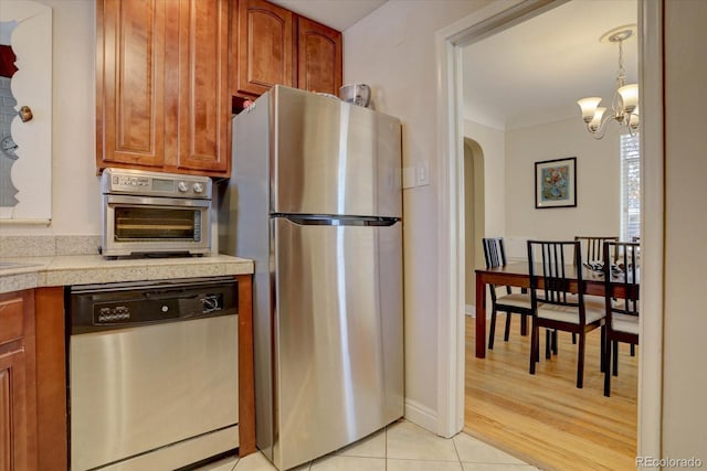 kitchen with pendant lighting, appliances with stainless steel finishes, an inviting chandelier, and light tile patterned floors