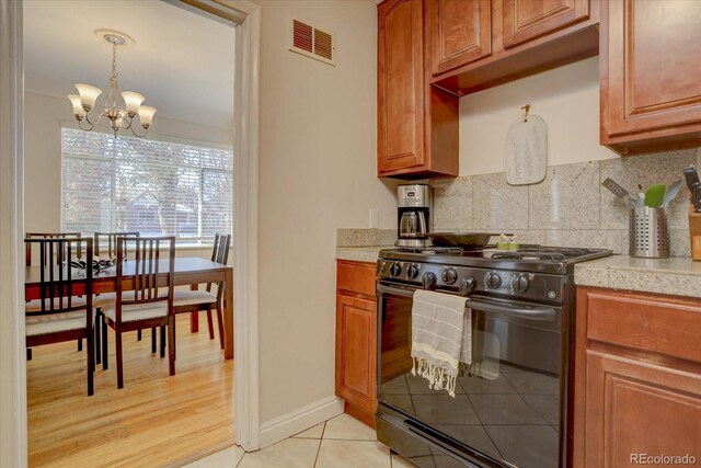 kitchen featuring decorative light fixtures, a chandelier, light tile patterned floors, black gas range oven, and decorative backsplash