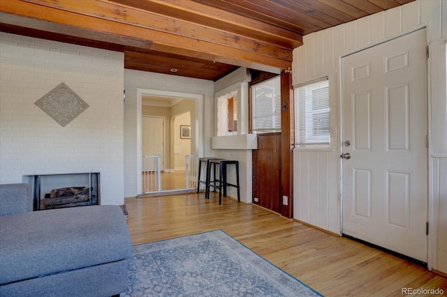 living room with beamed ceiling, a brick fireplace, wooden ceiling, and light hardwood / wood-style flooring