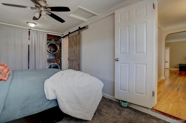 bedroom with ceiling fan, stacked washer / drying machine, a barn door, and wood-type flooring