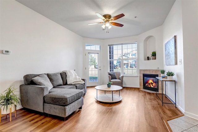 living room featuring ceiling fan, light hardwood / wood-style floors, and a tiled fireplace