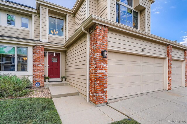 455 Bexley St, Littleton, CO 80126 - doorway to property featuring an attached garage, brick siding, and driveway