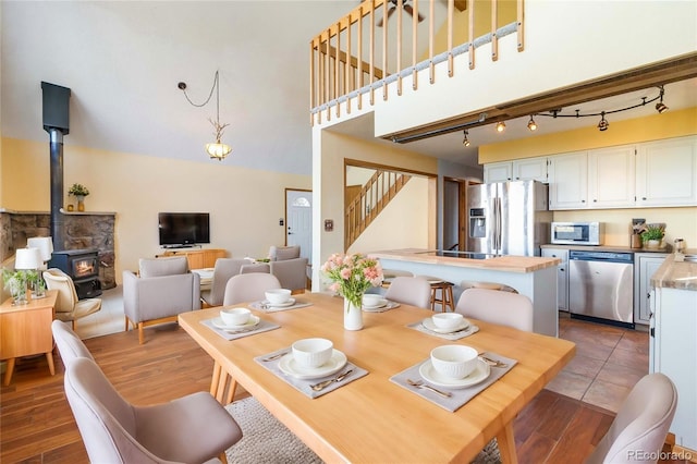 dining room featuring dark hardwood / wood-style flooring, a wood stove, rail lighting, and a towering ceiling