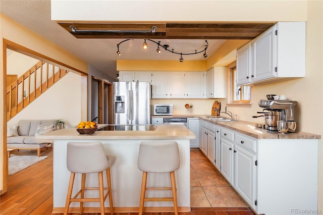 kitchen featuring white cabinets, stainless steel fridge, light wood-type flooring, and a kitchen bar