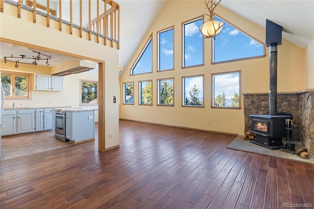 unfurnished living room featuring wood-type flooring, a textured ceiling, high vaulted ceiling, and a wood stove