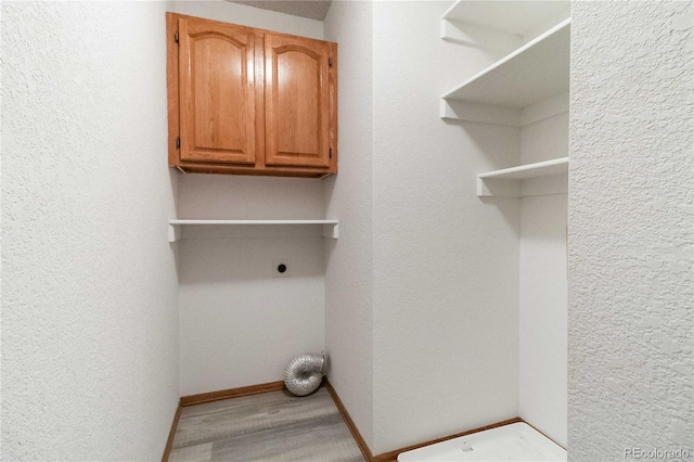 laundry room with electric dryer hookup, cabinets, and wood-type flooring