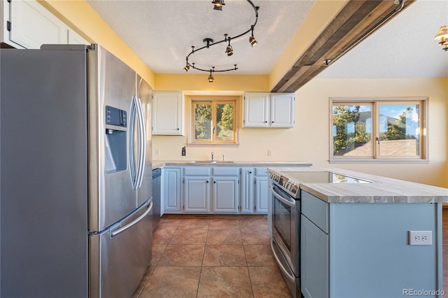 kitchen with appliances with stainless steel finishes, tile patterned floors, a textured ceiling, blue cabinetry, and white cabinetry