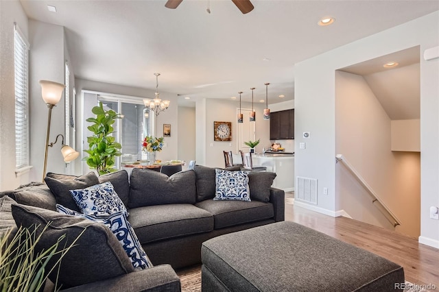 living room with ceiling fan with notable chandelier and light hardwood / wood-style floors