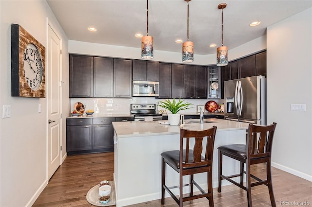 kitchen with dark brown cabinetry, hanging light fixtures, stainless steel appliances, and a center island with sink