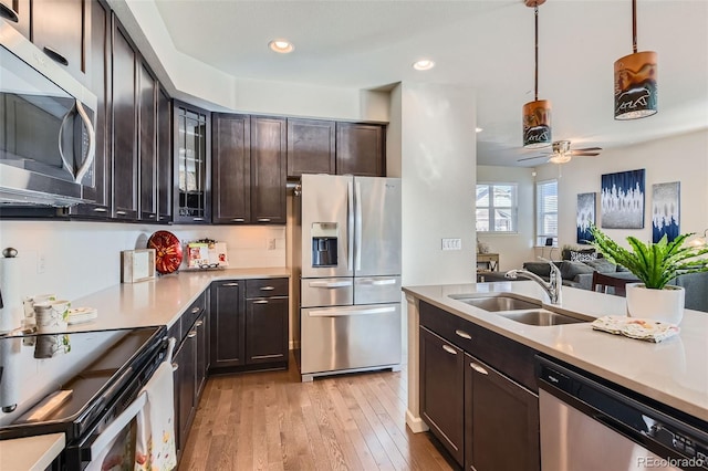 kitchen with sink, appliances with stainless steel finishes, dark brown cabinets, light hardwood / wood-style floors, and decorative light fixtures