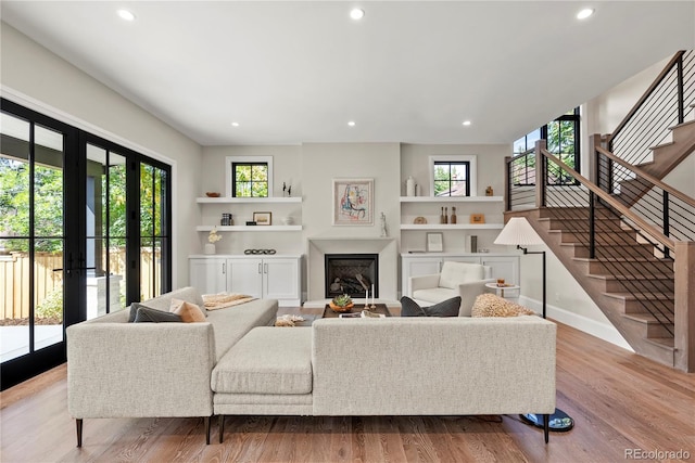 living room with built in shelves, a healthy amount of sunlight, and light hardwood / wood-style flooring