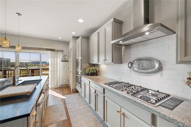 kitchen featuring appliances with stainless steel finishes, tasteful backsplash, a sink, light wood finished floors, and wall chimney exhaust hood