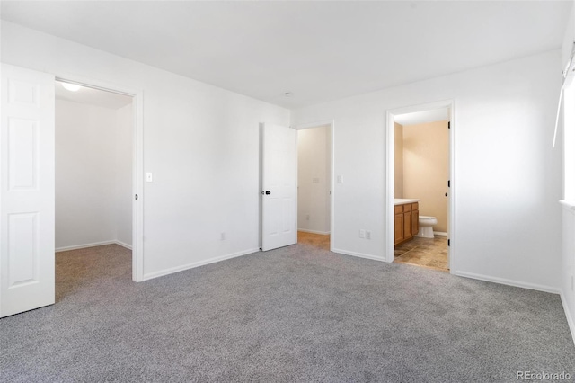 unfurnished bedroom featuring light colored carpet, ensuite bathroom, and a walk in closet