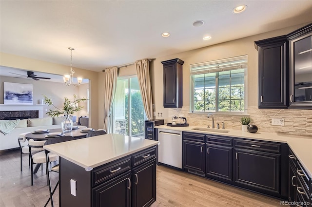 kitchen with stainless steel dishwasher, a sink, open floor plan, light countertops, and tasteful backsplash