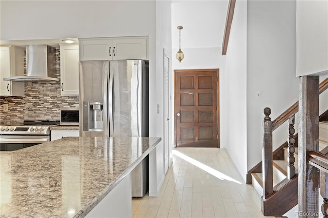 kitchen with decorative light fixtures, stainless steel appliances, decorative backsplash, light stone countertops, and wall chimney exhaust hood