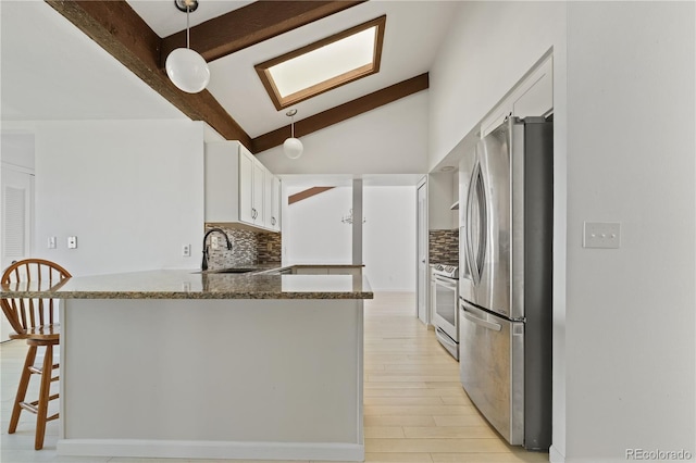 kitchen with white cabinetry, stainless steel appliances, a sink, vaulted ceiling with skylight, and a peninsula